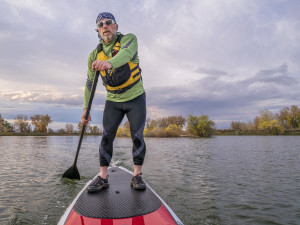 senior paddler in life jacket enjoying stand up paddling on lake